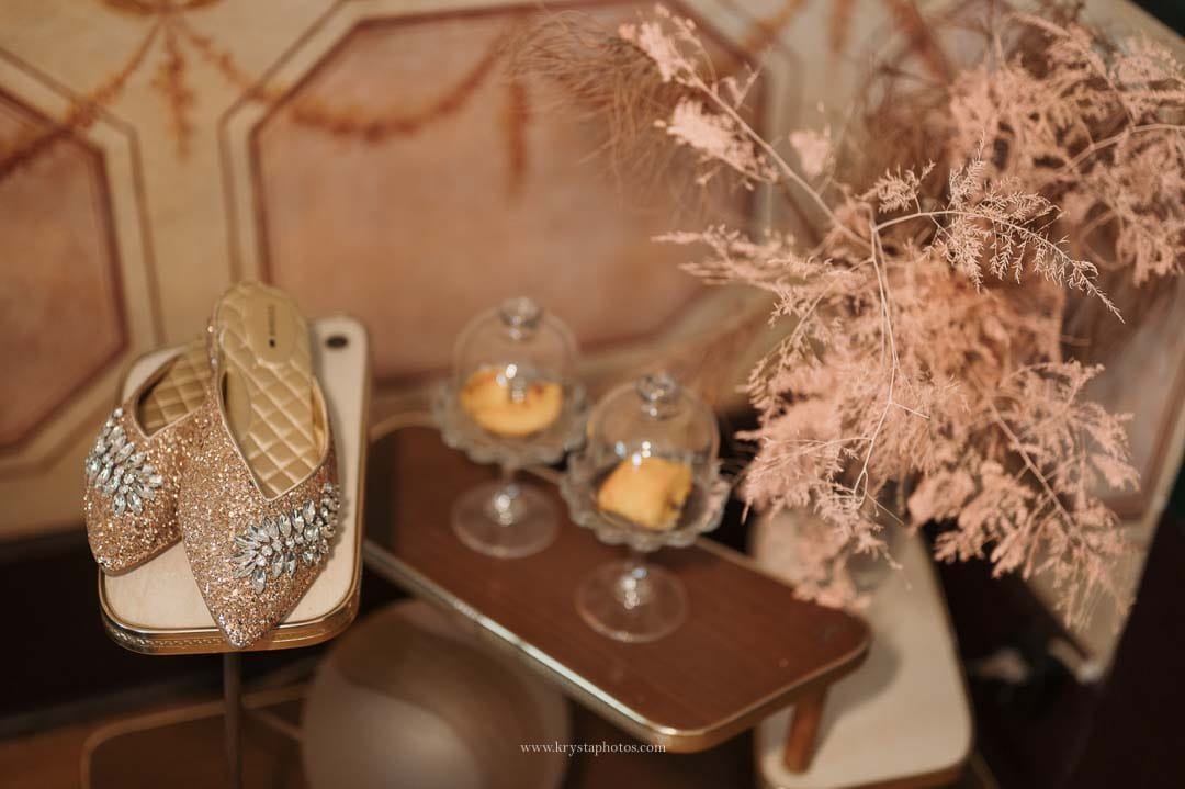 Bride’s shiny shoes beside traditional Portuguese pastries on a rustic terracotta wall background during an intimate Lisbon wedding.