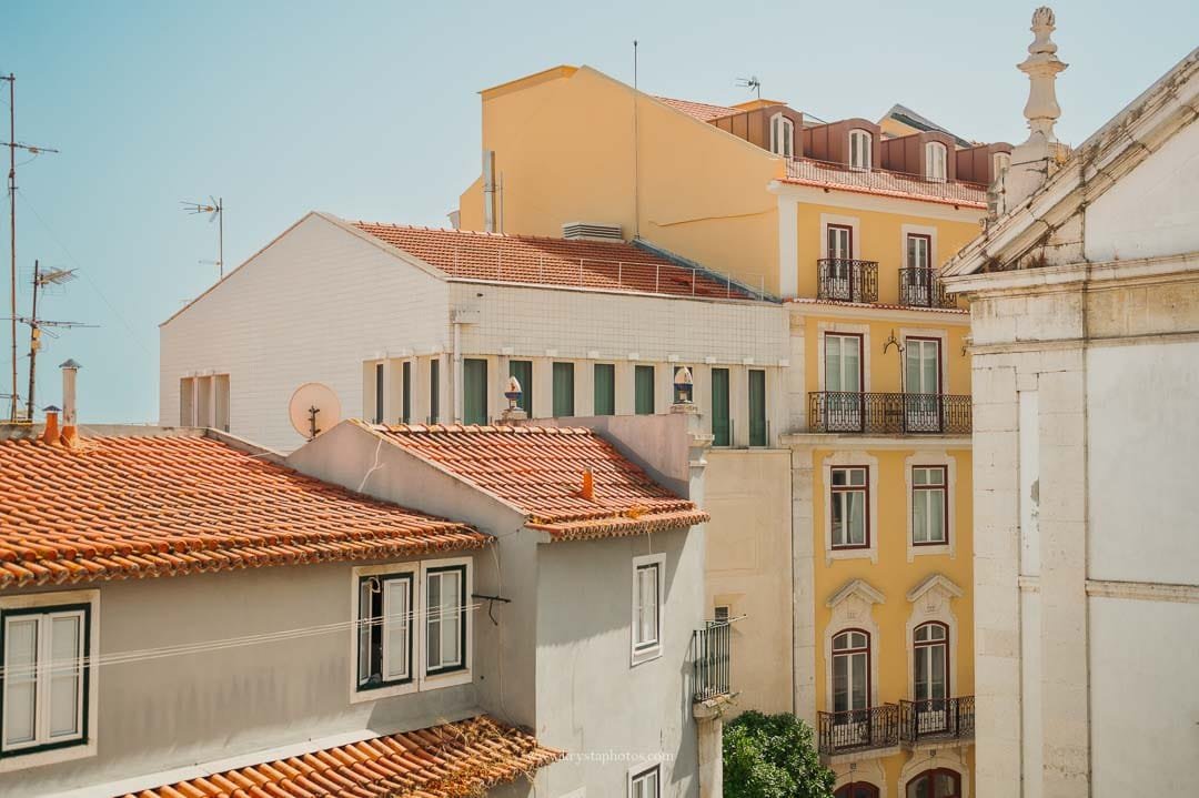View of pastel-colored Alfama houses in Lisbon with yellow and terracotta tones seen from a wedding Airbnb window.