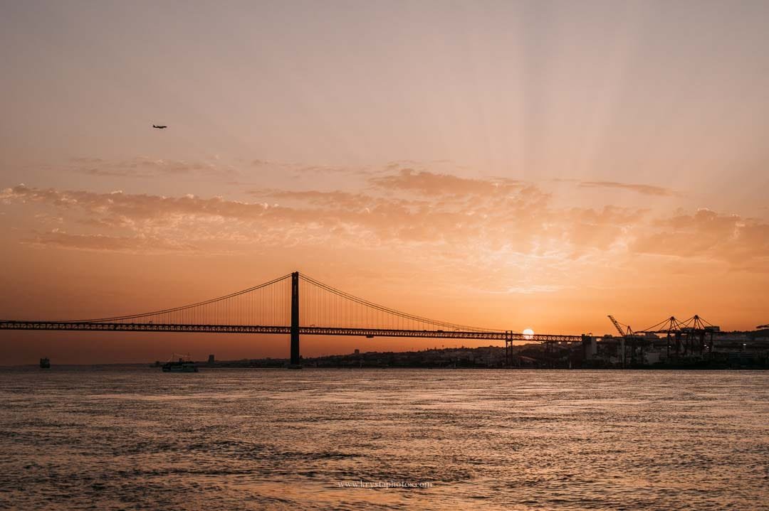 Sunset over the Tagus River in Lisbon with the bridge in view and a plane arriving, captured during an intimate micro-wedding sail.