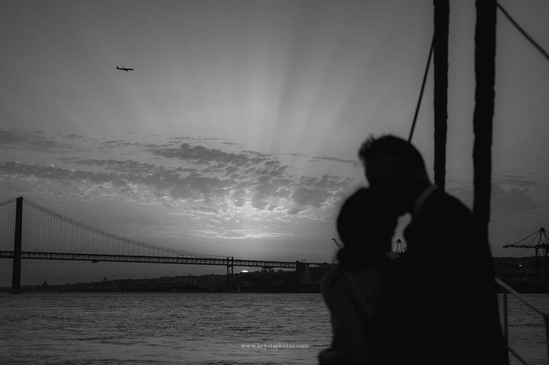 Sunset over the Tagus River in Lisbon with the bridge in view and a plane arriving, captured during an intimate micro-wedding sail.
