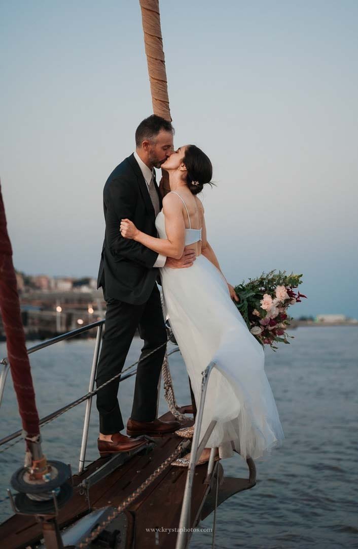 Bride and groom kissing on a sailboat during their sunset cruise in Lisbon after their intimate micro-wedding.