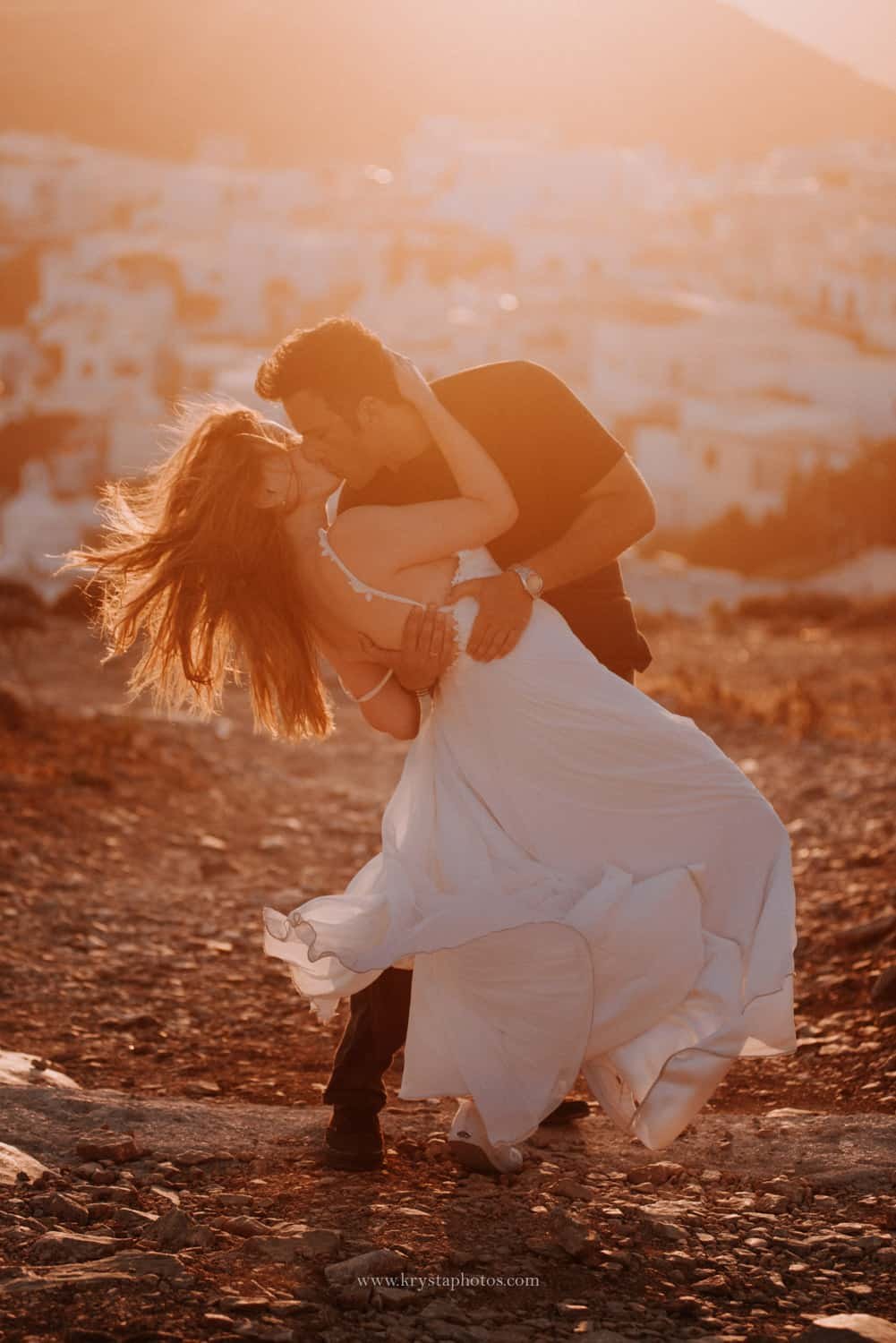 Couple kissing at sunset overlooking the whitewashed village of Amorgos, Greece during a romantic engagement session
