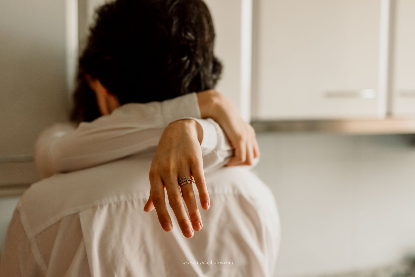 Close up maternity photo of an expecting couple embracing in their kitchen, with the mother’s hand resting gently on the partner’s shoulder, captured indoors using natural light in a documentary style.<br />
