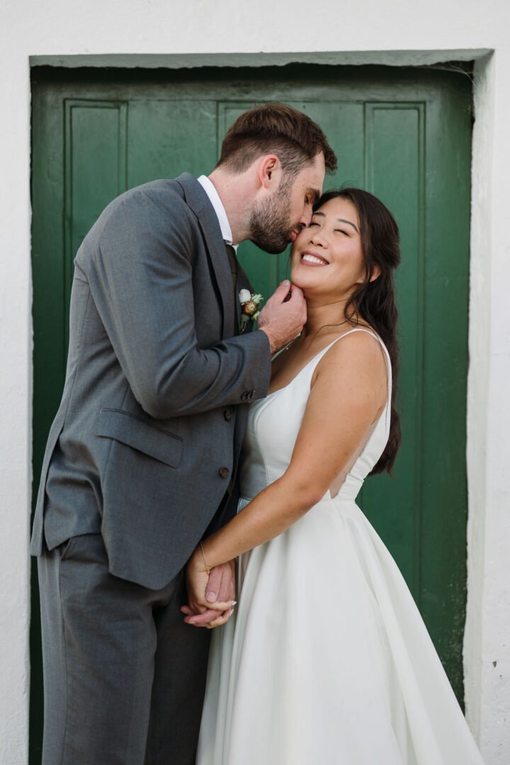Bride and groom sharing an intimate moment during their wedding day, standing in front of a green door, holding hands and smiling