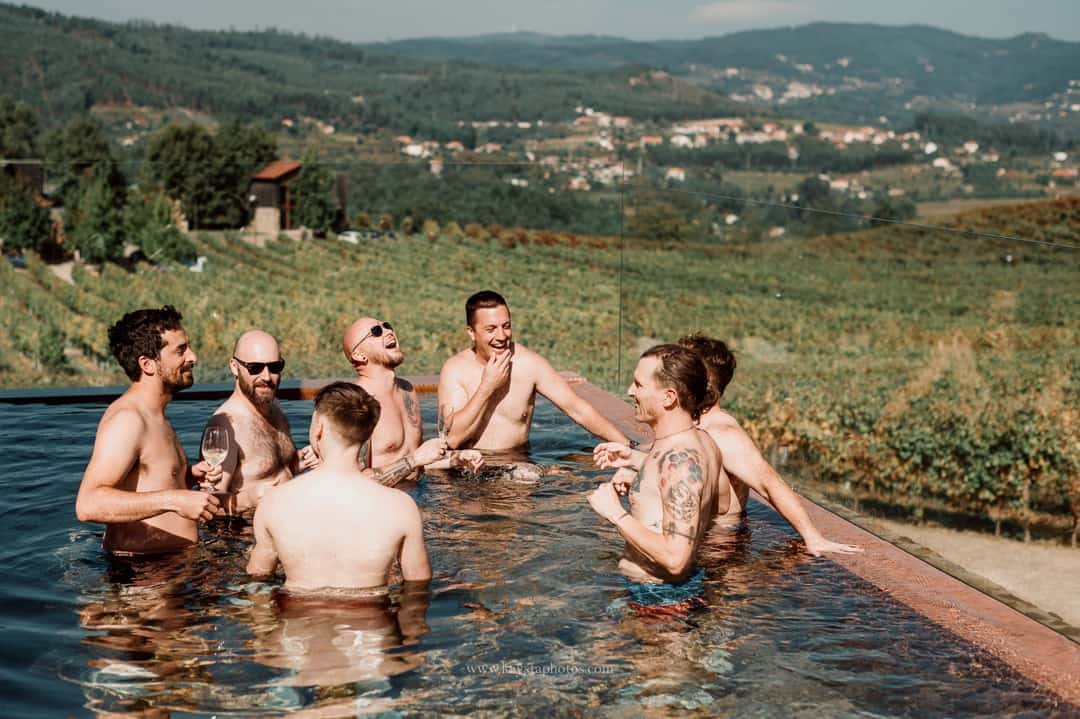 Groom and groomsmen relaxing in a pool surrounded by lush green vineyards during a whimsical Portugal wedding