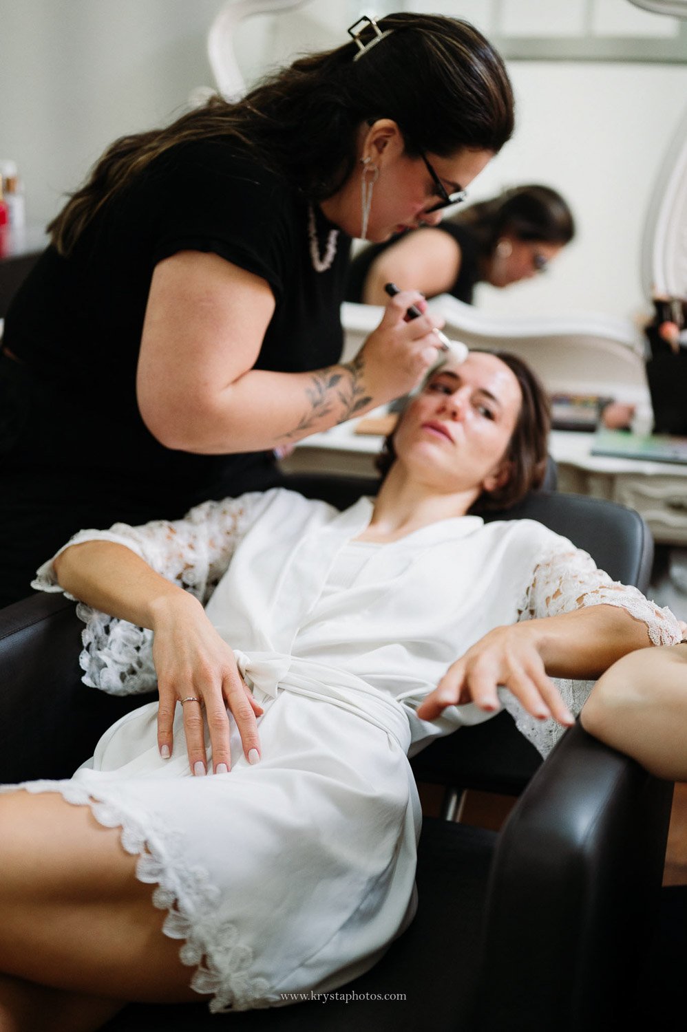 Bride wearing white silk robe with lace trim during bridal prep