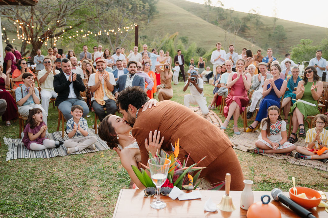 Bride and groom sharing their first kiss during an outdoor wedding ceremony in Portugal, surrounded by seated guests celebrating