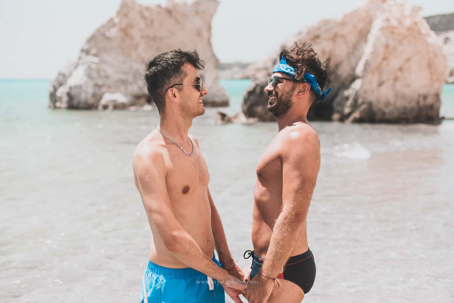 Happy gay couple smiling at each other on a sunny beach in Milos, Greece