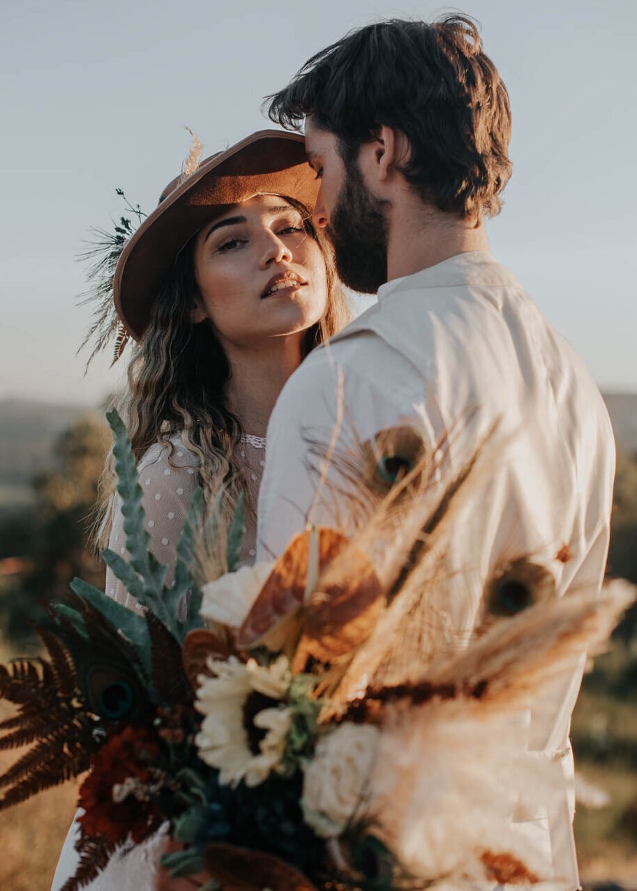 Bride in boho lace wedding dress holding wildflower bouquet in golden dry grass field, Greece