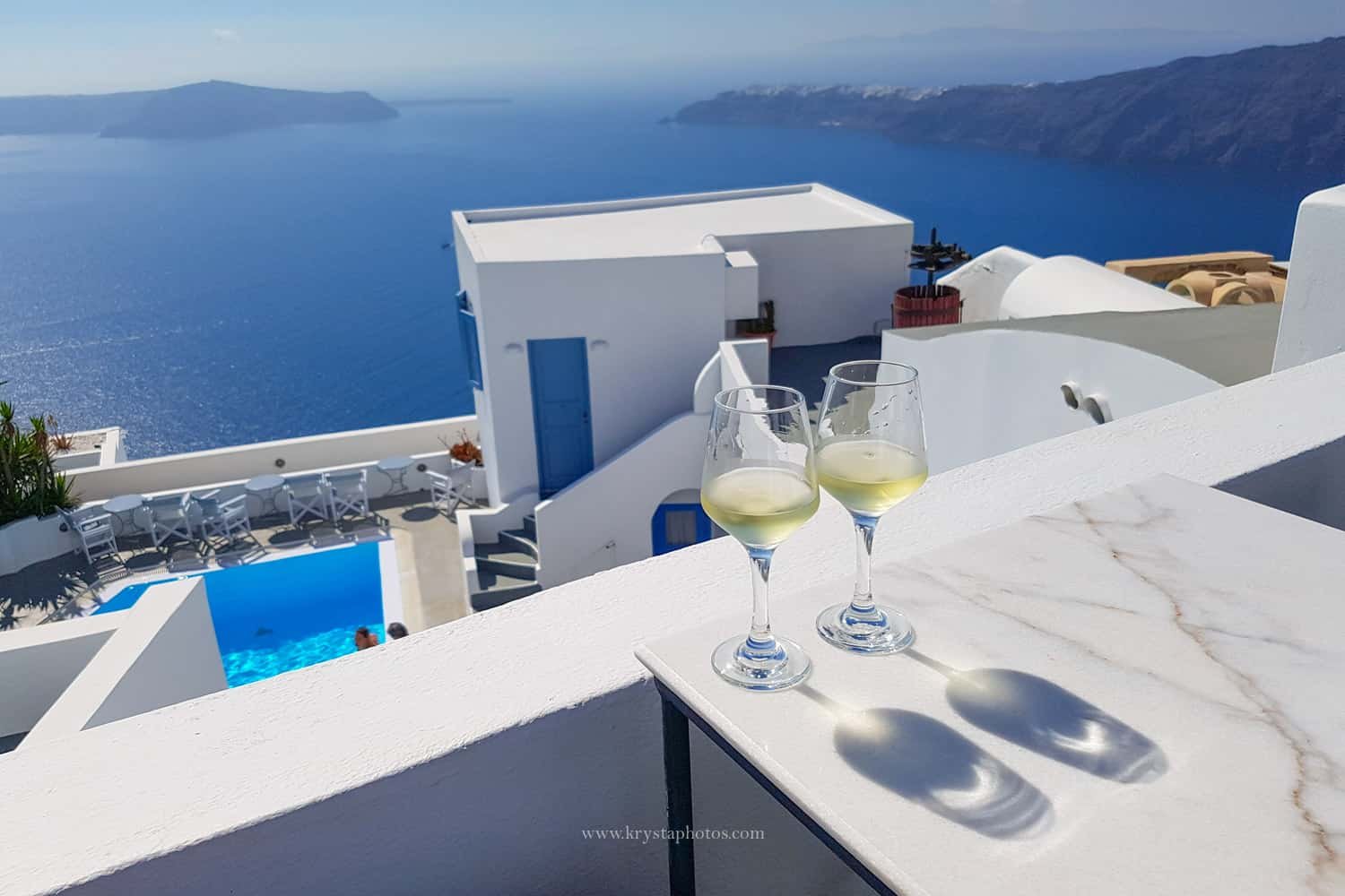 Two glasses of white wine on a balcony overlooking the Aegean Sea in Santorini, Greece