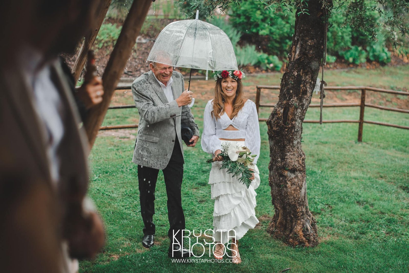 Bride walking down the aisle in the rain, her father shielding her hair with an umbrella, muddy sandals, candid joyful moment