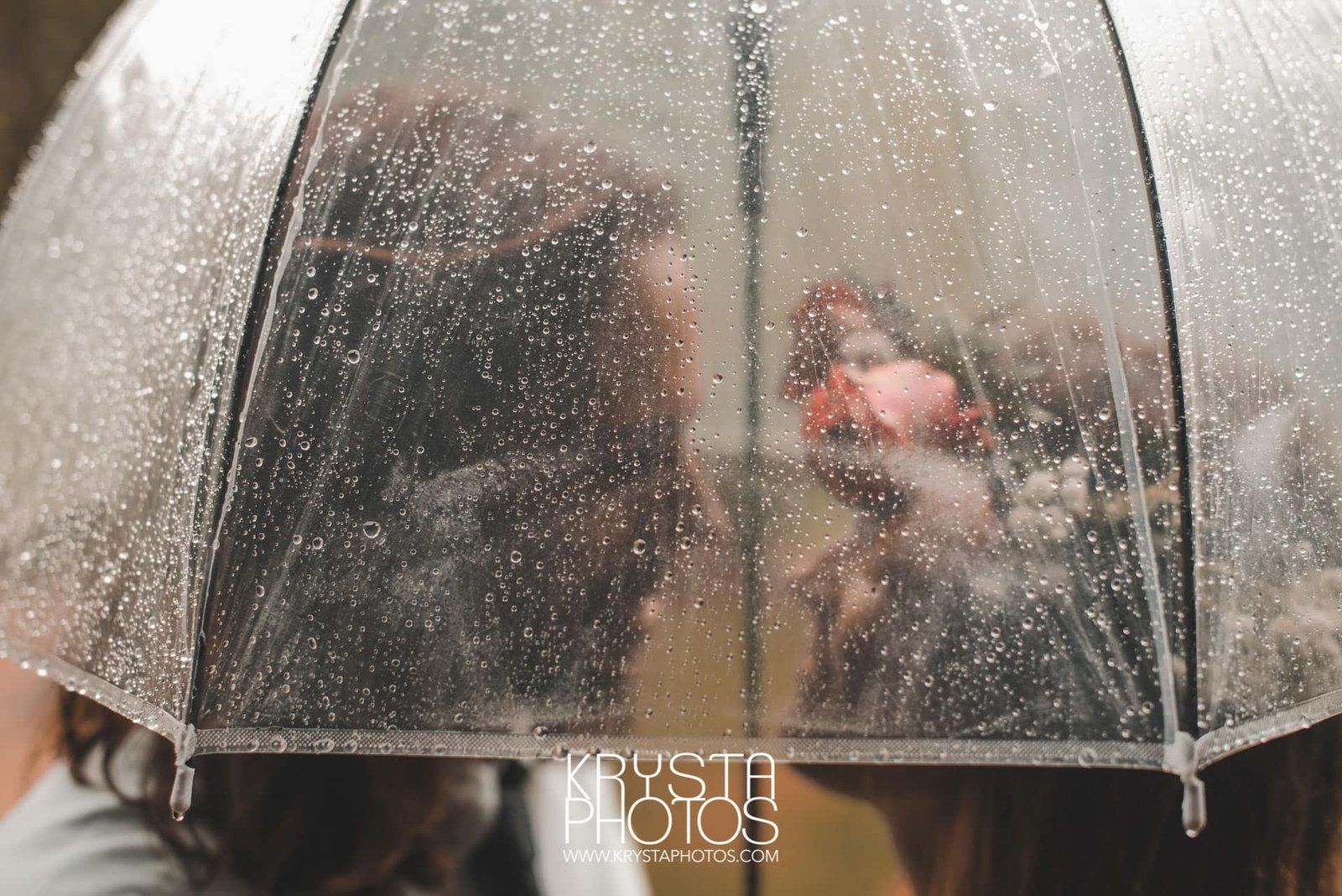 Cinematic closeup of bride and groom under a transparent umbrella with raindrops on their rainy wedding day