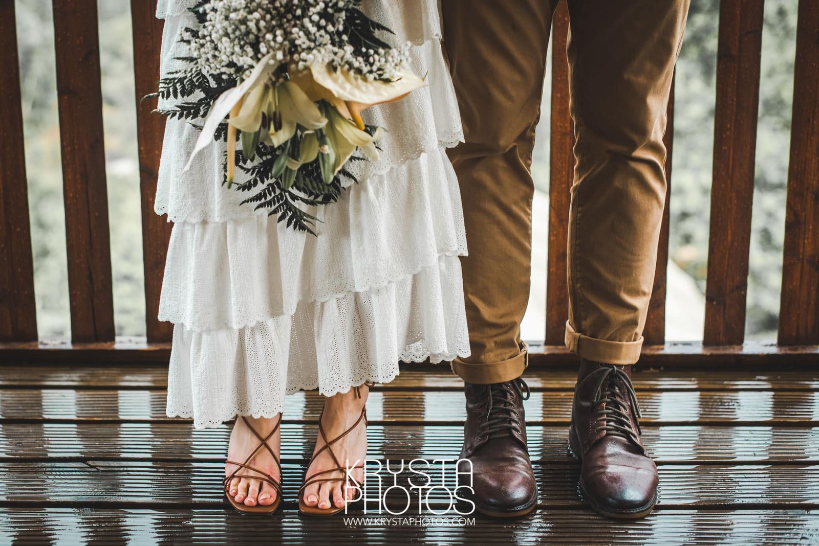 Bride and groom grinning under rain-soaked wedding ceremony, bride’s father shielding her hair with an umbrella, muddy sandals, candid joyful moment