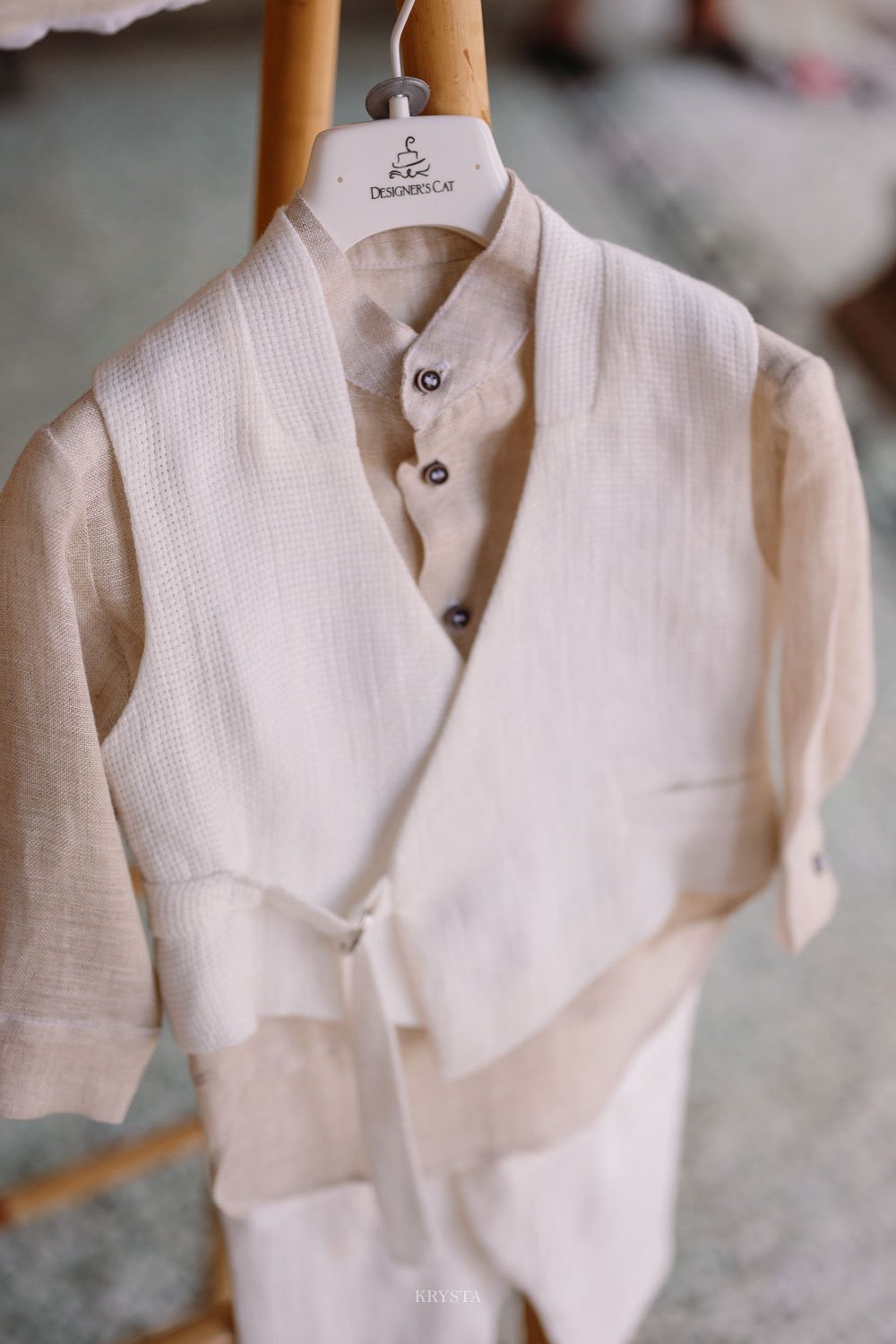 Cream linen and waffle-weave outfit by Designer's Cat hanging on a branded wooden hanger before a celebration in Limnos, Greece